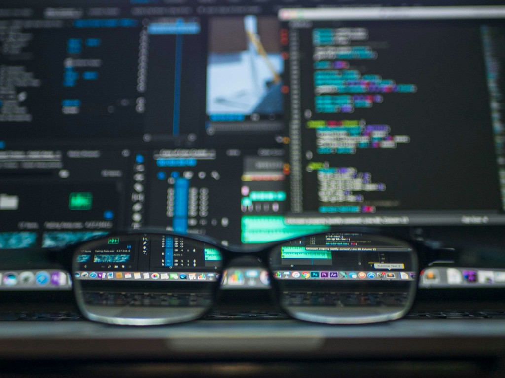 Glasses resting on a laptop with code and creative software on screen
