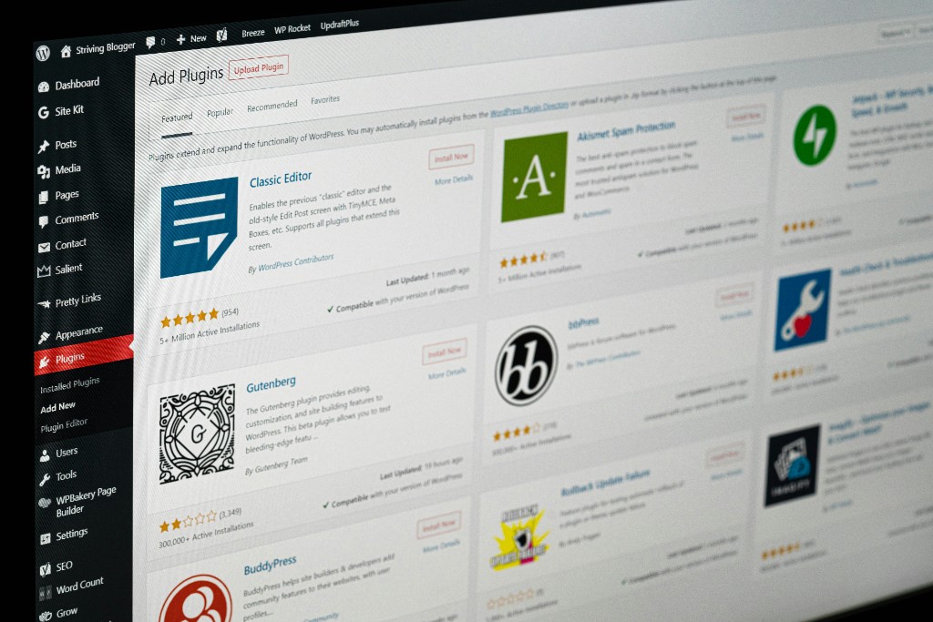 WordPress admin Plugins screen on a monitor, showing the plugin management burden